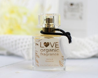 May include: A clear glass bottle of LOVE organic fragrance with a black cap and a white heart-shaped charm. The bottle is labeled with the text "LOVE organic fragrance" and "Vanilla & Opoponax" in gold lettering. The bottle contains 30 ml of eau de parfum.