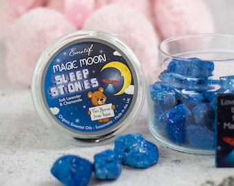 May include: A glass jar filled with blue sleep stones, labeled "Magic Moon Sleep Stones" with the text "Soft Lavender & Chamomile, Organic Essential Oils - Sustainable - Made in the UK".