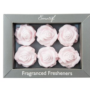 May include: A box containing six pink rose-shaped air fresheners. The box is grey with the text "Emotif" and "Fragranced Fresheners" printed on it.