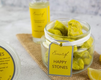 May include: A glass jar filled with yellow and green bath salts labeled "Emotif Happy Stones".