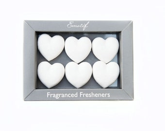 May include: A gray box with the word "Emotif" printed on the top and the words "Fragranced Fresheners" printed on the bottom. The box contains six white heart-shaped air fresheners.