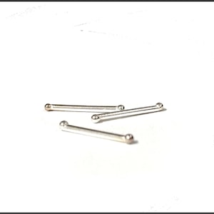 May include: Four small, silver metal bars, each with a ball at either end, are arranged on a white background. These straight bars could be jewellery components or findings.
