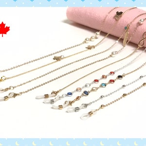 May include: Eyeglass chains in gold and silver hues, featuring charms like pearls, a butterfly, and an infinity symbol. The chains have loops for glasses and are displayed on a pink surface.