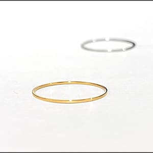 May include: Two thin rings, one gold and one silver, are displayed against a white background. The gold ring is in the foreground, and the silver ring is slightly out of focus in the background. The rings are simple and elegant.