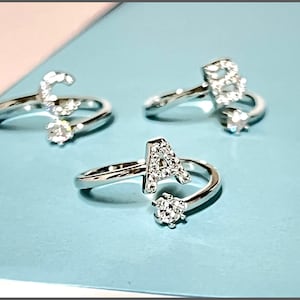 May include: Three silver adjustable rings, each with a different letter: "C", "B", and "A". The letters are set with small, clear crystals. Each ring has a sparkling, round crystal accent.