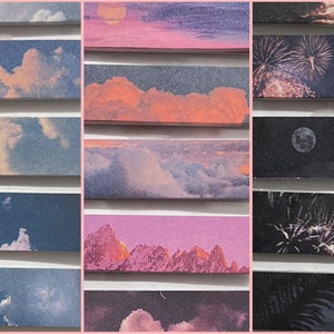 May include: A collection of rectangular stickers featuring various landscape scenes. The stickers depict clouds, sunsets, mountains, fireworks, and the moon. The color palette includes blues, pinks, oranges, and purples, creating a dreamy aesthetic.