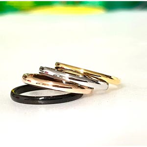May include: Five thin rings in a range of colours: black, rose gold, silver, and gold. The rings are slightly stacked, displaying their smooth, polished surfaces. The rings are a simple, elegant design.