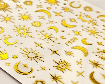 May include: Sheet of gold foil stickers featuring celestial designs. The stickers include suns, moons, stars, and other cosmic shapes. The stickers have a glossy finish and are arranged on a white background. The text "F908" is visible on the sheet.