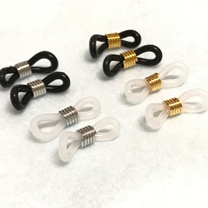 May include: Eyeglass retainers in black and white, with silver and gold-coloured metal accents. The retainers are made of a flexible, rubber-like material and are designed to loop around the temples of eyeglasses.