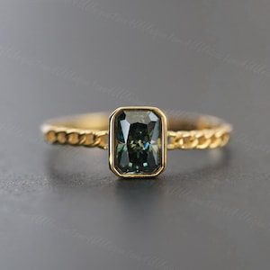 May include: A gold ring with a dark green emerald-cut gemstone set in a bezel setting. The band is a twisted rope design.