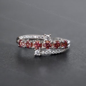 May include: A silver ring featuring a row of small pink gemstones and a row of smaller clear gemstones.