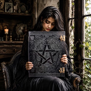 May include: A rectangular black leather-bound book featuring an embossed pentagram design on the front cover, surrounded by intricate floral patterns. The book is secured with two metallic brass-colored latches on the right side edge.