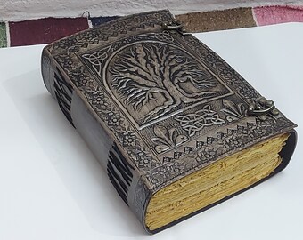 May include: A brown leather journal with a tree of life design embossed on the cover. The journal has a Celtic knot design and is closed with two metal clasps.