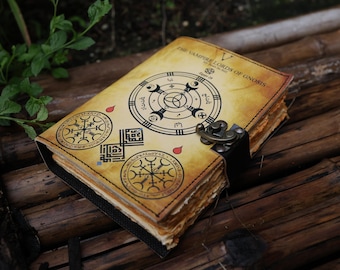 Peut inclure: Un journal relié en cuir d'aspect vintage. La couverture présente des symboles noirs et blancs complexes et le texte "The Vampire Lords of Gnomes". Le journal a un fermoir en métal et est fermé.