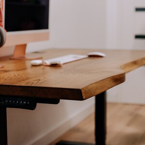 K&ouml;nnte beinhalten: Ein Holzschreibtisch mit einer Live-Edge-Oberfl&auml;che und schwarzen verstellbaren Beinen. Der Schreibtisch hat eine wei&szlig;e Maus und eine Tastatur. Der Schreibtisch befindet sich in einem Heimb&uuml;ro.