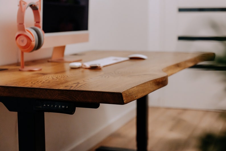 K&ouml;nnte beinhalten: Ein Holzschreibtisch mit einer Live-Edge-Oberfl&auml;che und schwarzen verstellbaren Beinen. Der Schreibtisch hat eine wei&szlig;e Maus und eine Tastatur. Der Schreibtisch befindet sich in einem Heimb&uuml;ro.