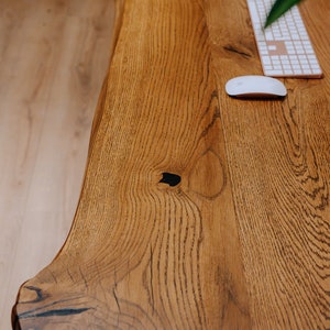 K&ouml;nnte beinhalten: Nahaufnahme eines Holzschreibtisches mit nat&uuml;rlicher Holzmaserung. Der Schreibtisch hat eine wei&szlig;e kabellose Tastatur und Maus darauf. Der Schreibtisch besteht aus einem einzigen St&uuml;ck Holz mit einer lebenden Kante.