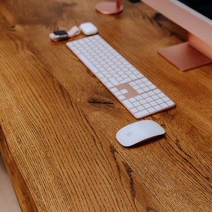 K&ouml;nnte beinhalten: Ein Holzschreibtisch mit einer wei&szlig;en kabellosen Tastatur, einer wei&szlig;en kabellosen Maus und einem rosa Kopfh&ouml;rerst&auml;nder mit rosa Kopfh&ouml;rern.