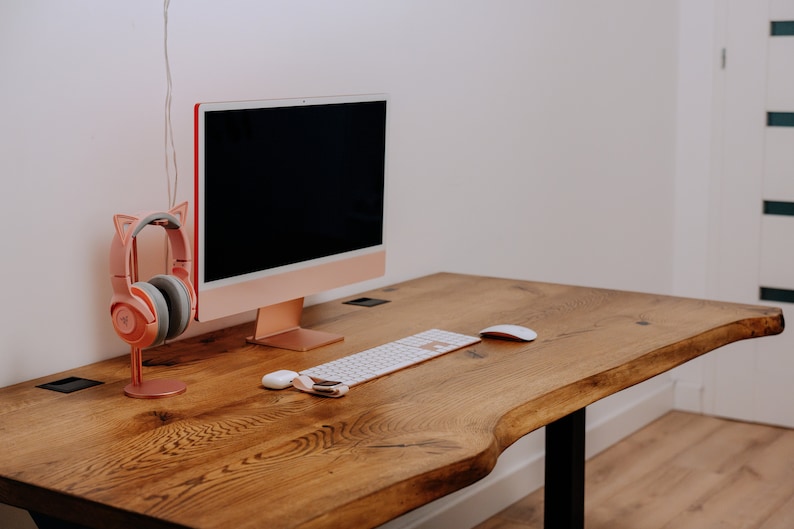 K&ouml;nnte beinhalten: Ein Holzschreibtisch mit einer hellen Holzoptik. Auf dem Schreibtisch stehen ein Computermonitor, eine Tastatur und eine Maus. Links neben dem Monitor steht ein rosa Headset mit Katzenohren auf einem St&auml;nder.