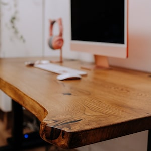 K&ouml;nnte beinhalten: Nahaufnahme eines Holztisches mit einer lebenden Kante. Der Tisch ist aus nat&uuml;rlichem Holz in einem satten Braunton gefertigt. Der Tisch ist scharf, w&auml;hrend der Hintergrund unscharf ist.