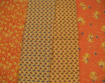 Peut inclure: Quatre bandes de tissu aux motifs distincts : un imprimé floral orange, un tissu crème à motif géométrique bleu et rouge, un tissu crème à motif géométrique violet et vert, et un tissu orange orné de petits chatons illustrés.