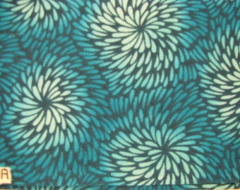 Könnte beinhalten: Ein Stoff mit einem sich wiederholenden Muster aus stilisierten, kreisförmigen Blumenformen in Blaugrün-, Türkis- und Weißtönen. Das Design besteht aus strahlenförmigen, blütenblattartigen Strichen, die einen dichten, geschichteten Effekt erzeugen.