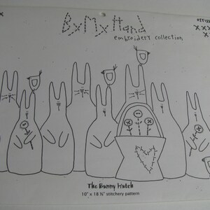 May include: A white paper sheet featuring the By My Hand embroidery collection pattern titled The Bunny Hutch. The black line drawing depicts a group of rabbits, birds, and a basket with flowers. The text 10" x 18 1/2" stitchery pattern is printed at the bottom.