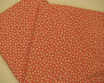 Peut inclure: Gros plan sur un tissu corail avec un motif répétitif de petits carrés blanc cassé. Chaque carré a un petit point au centre, avec des points supplémentaires bleus et verts. Le tissu est plié, montrant sa texture et son design.