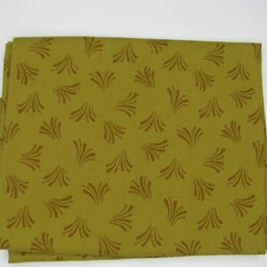 May include: Folded fabric with a repeating pattern of brown fan-like shapes on a green background. The fabric is folded neatly, showcasing the pattern's design. The fabric appears to be cotton or a similar material.