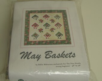 Könnte beinhalten: Ein Quilt-Muster-Set mit dem Titel May Baskets von Billie Mahorney für The Pine Needle, verpackt in einer transparenten Plastiktüte. Das Cover zeigt ein 122 cm mal 122 cm großes Quilt-Design mit einem Gitter aus Blumenkörben.