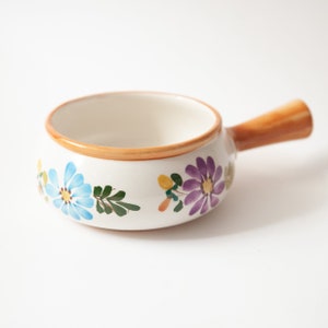May include: A white ceramic serving dish with a brown handle and floral designs in shades of blue, purple, green, and yellow.
