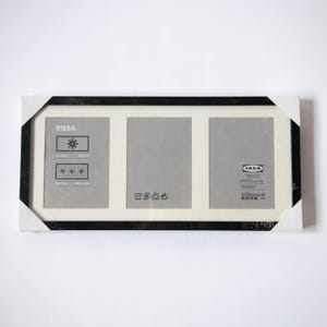 May include: A black picture frame with three openings for photos. The frame is labeled "RIBBA" and "IKEA".