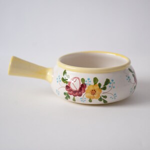 May include: A white ceramic serving dish with a yellow rim and floral design. The dish has a handle and is perfect for serving sauces, dips, or desserts.