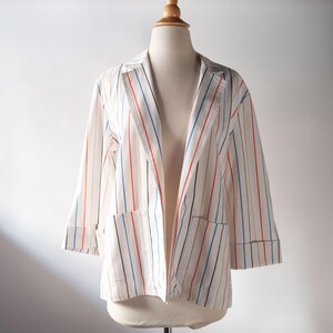 May include: A white striped blazer with blue, red, and black stripes. The blazer has a collar and two pockets.