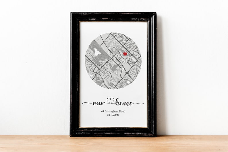 May include: A black framed print with a gray and white map of a neighborhood. A red heart marks a location on the map. The text "our home" is written in cursive below the map with the address "65 Bassingham Road" and the date "02.10.2021" below the text.