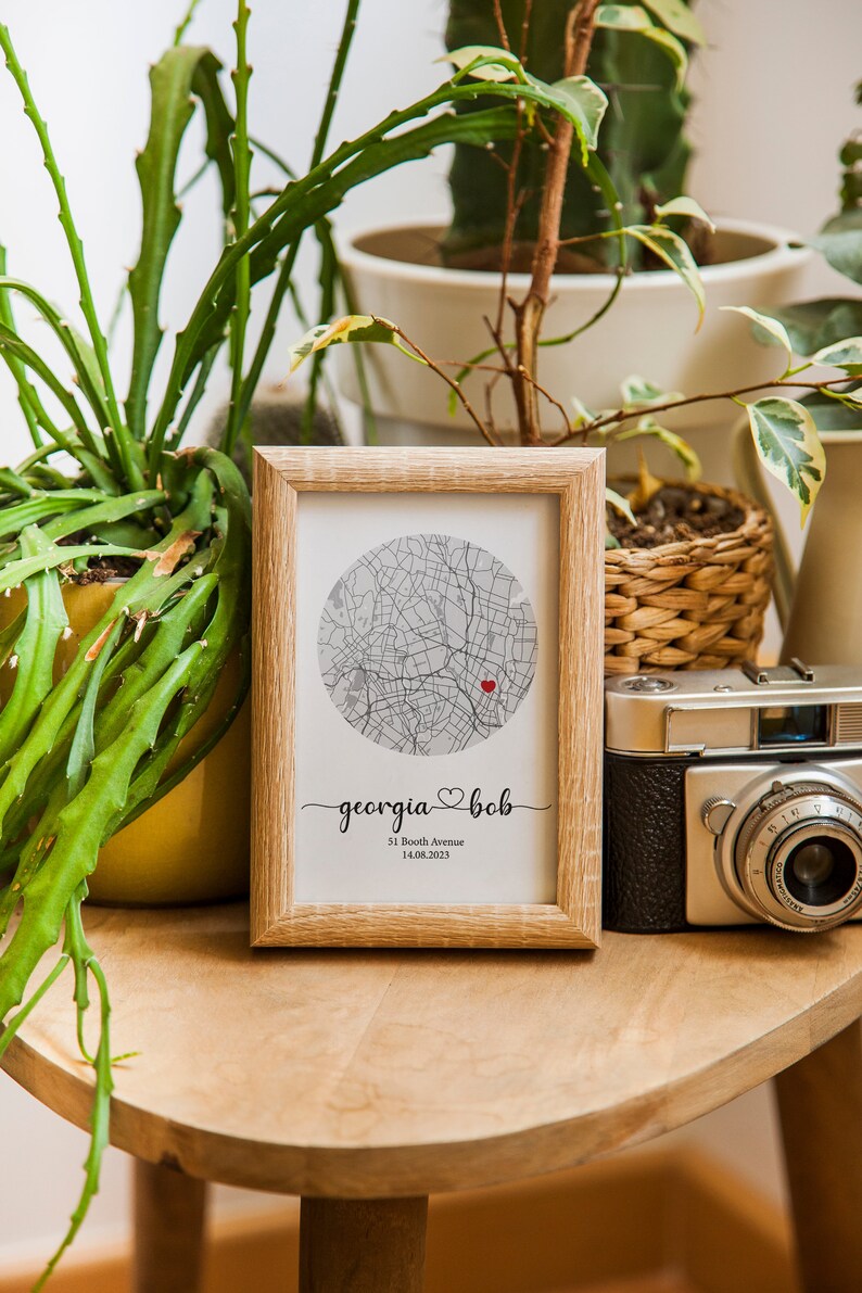 May include: A framed print with a map of a city in a circle. The map is in black and white with a red heart marking a location. The text below the map reads "georgia &hearts; bob 51 Booth Avenue 14.08.2023".