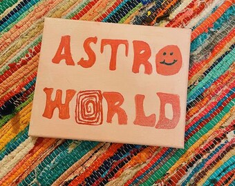 Könnte beinhalten: Eine rosa Leinwand mit den Worten "ASTRO WORLD" in Rot bemalt. Ein rotes Smiley-Gesicht ist rechts neben dem Wort "ASTRO" gemalt.
