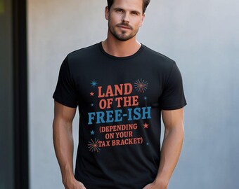 May include: A black short-sleeved t-shirt featuring the red and blue text 'LAND OF THE FREE-ISH (DEPENDING ON YOUR TAX BRACKET)' printed on the chest, accented with small red and blue star and firework graphic elements.