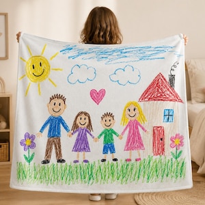 May include: A white fleece blanket featuring a colourful child's drawing of a family of four holding hands in front of a house. The illustration includes a yellow sun, blue clouds, a pink heart, green grass, and two flowers in vibrant crayon colours.
