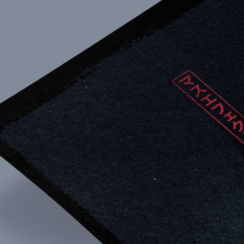 May include: A dark blue rectangular textile with a black border. The upper right corner features red Japanese characters within a rectangular frame. The textile has a textured surface and is set against a gray background.