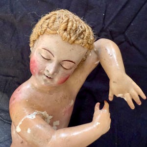 May include: Vintage bisque doll with closed eyes, rosy cheeks, and blonde, curly hair. The doll's arms are outstretched, and the paint is chipped in places, revealing the bisque underneath. A collectible item.