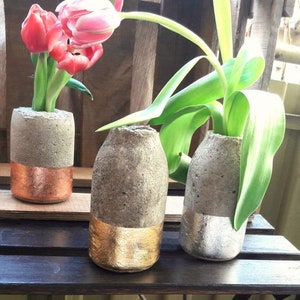 Può includere: Tre vasi in cemento con accenti dorati e argentati. I vasi sono riempiti con tulipani rosa e piante verdi.