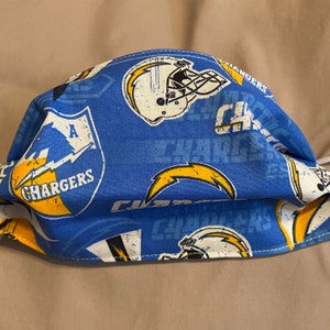 May include: A blue and yellow face mask with a repeating pattern of the Los Angeles Chargers logo. The logo features a lightning bolt and the words "Chargers".