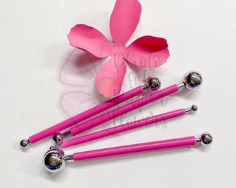 May include: Four pink-handled tools with different sized ball-shaped tips. The tools are used for creating paper flowers.