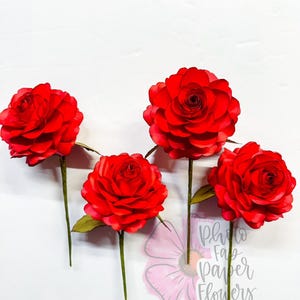 May include: Five vibrant red paper roses with green stems and leaves are arranged against a white background. The flowers have multiple layers of petals, creating a full, realistic appearance. The stems are long and slender.