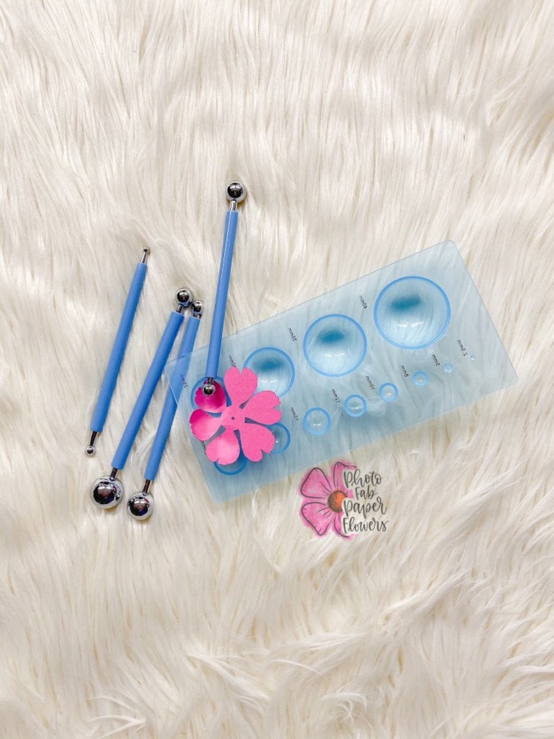 May include: A set of four blue tools with round metal tips and a blue plastic template with multiple circular cutouts. The template has a pink paper flower on it. The text "Photo Fab Paper Flowers" is visible on the template.