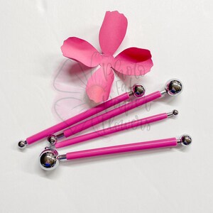 May include: Four pink handled tools with different sized ball-shaped tips. The tools are used for creating paper flowers.