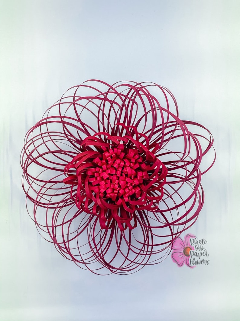 May include: A large, burgundy paper flower with a layered, circular design. The flower is made of many thin strips of paper that are curled and layered to create a 3D effect. The flower is centered in the image and is the only object present.