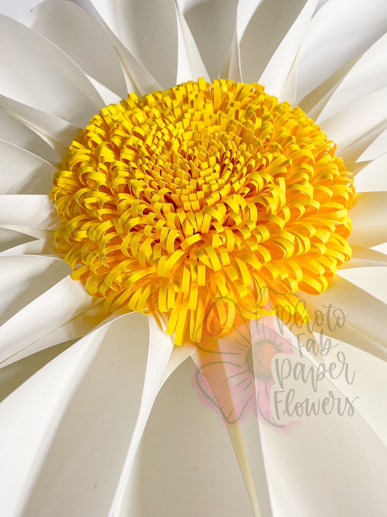 May include: A large white paper daisy with a yellow paper center. The center is made of many curled paper strips. The daisy is a paper flower.