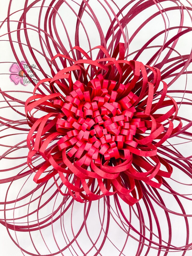 May include: A large, red paper flower with a layered, ruffled center. The flower is made from strips of paper that are curled and layered to create a 3D effect.